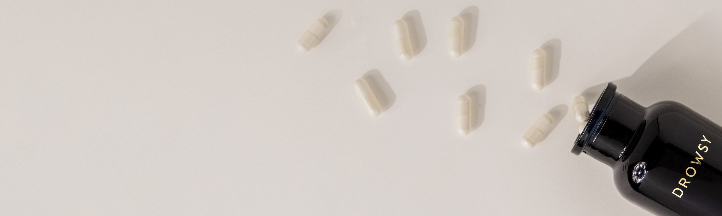 A black bottle labeled DROWSY tipped over on a light surface, with several white capsules spilling out.
