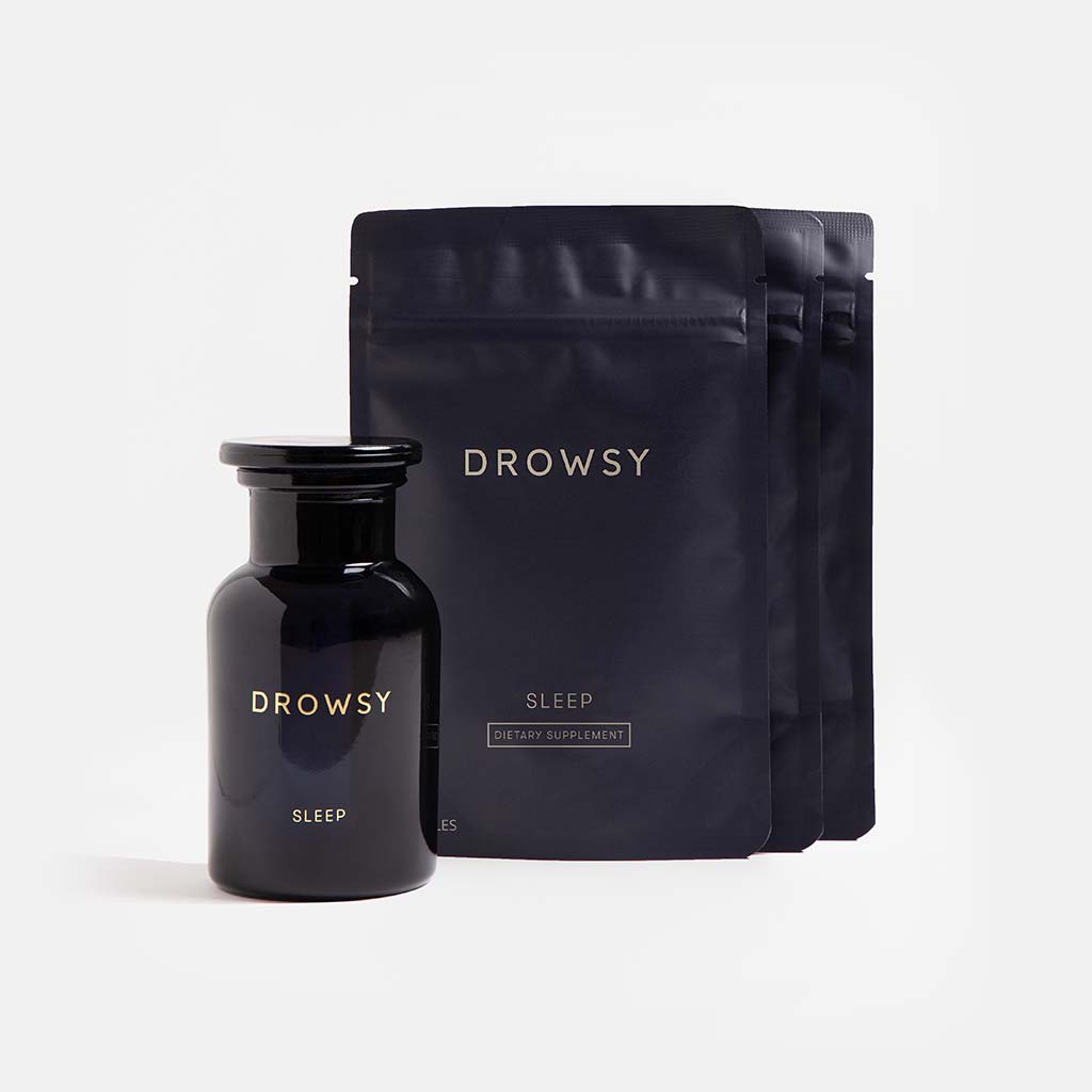 A dark glass bottle labeled Supplements - Sleep stands before three black resealable pouches with us.drowsysleepco branding on a white background, showcasing this nightly supplement designed to promote relaxation and support restful sleep.