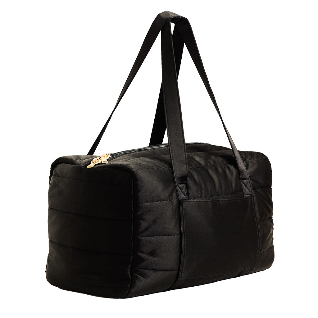 The Drowsy Silk Weekender - Black Jade by Drowsy is a black quilted bag with two long handles, a side pocket, and gold-tone zippers—ideal for travel essentials. Shown here against a white background.