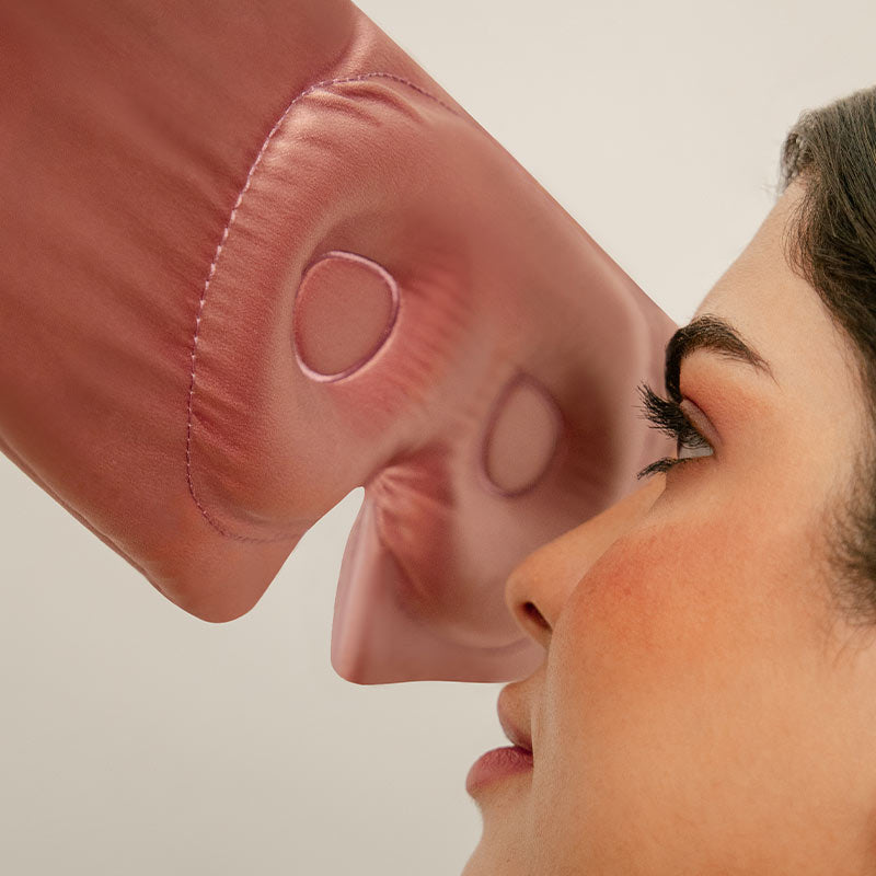 A close-up of a woman’s face facing a large, flesh-toned boxing glove, which is gently pressed against her nose. The background is plain and neutral.