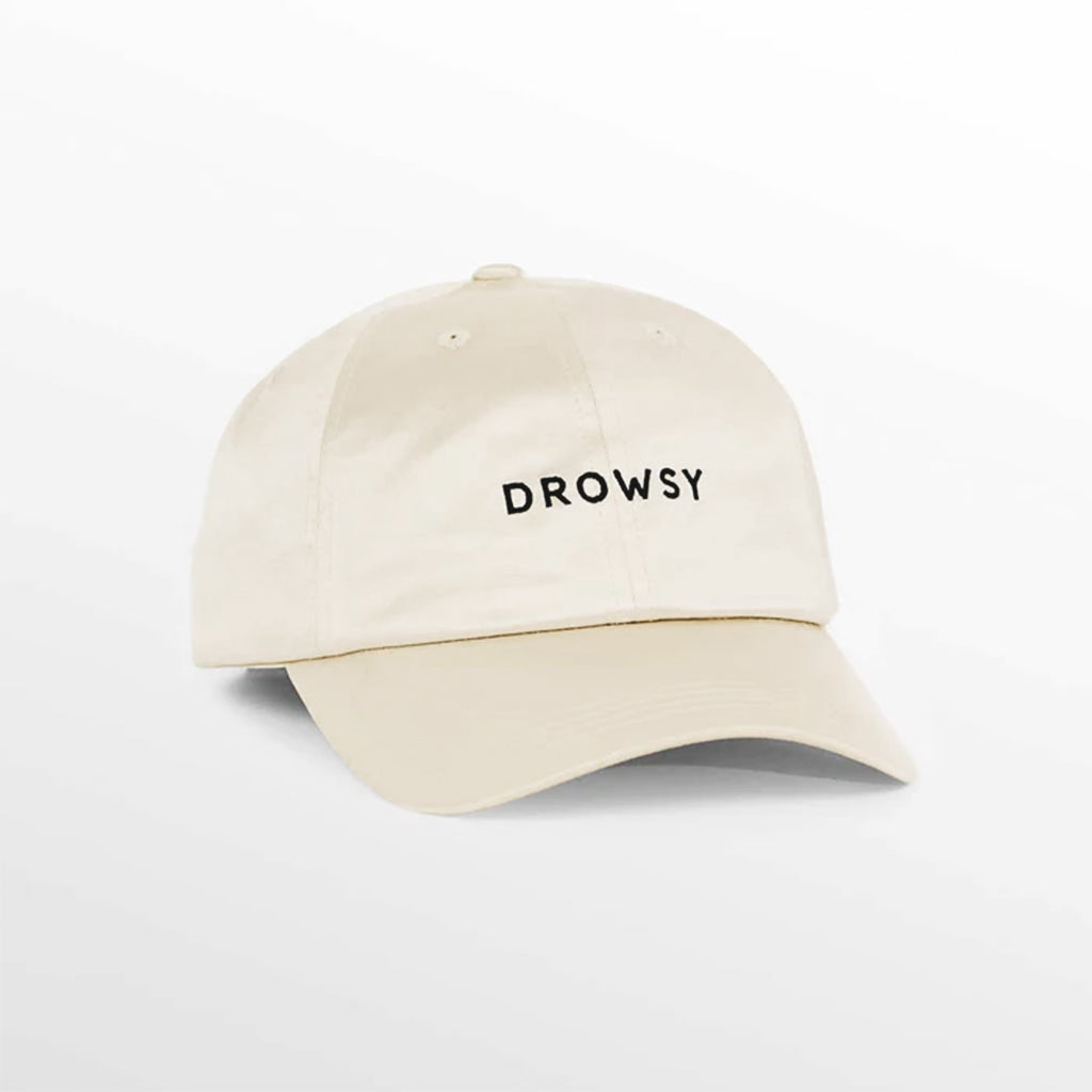 The Drowsy Silk Cap in Dusty Gold by Drowsy features "DROWSY" embroidered in black on the front, offering stylish sun protection. Shown against a soft, gradient background.