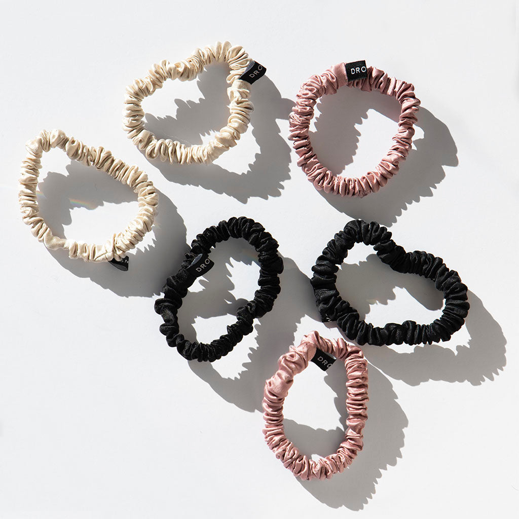 The us.drowsysleepco Skinny Scrunchie Set - Rose, Dusty, Black features six 22 momme silk scrunchies—two each in rose, dusty pink, and black—arranged on a white surface with subtle shadows for stylish, hair-friendly accessorizing.