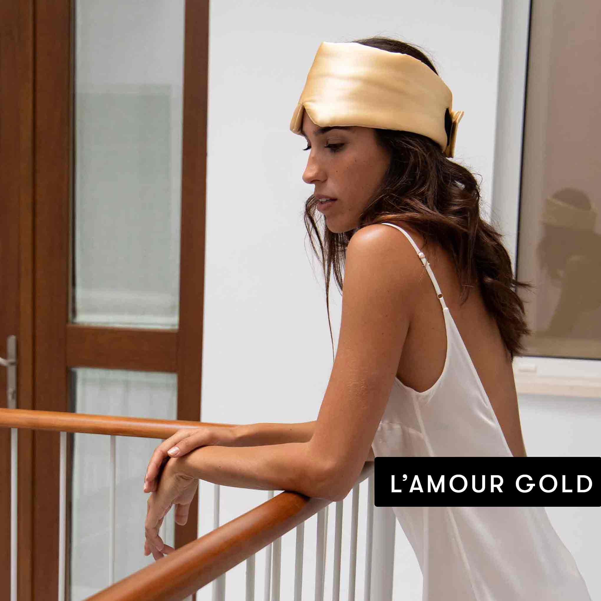 A woman in a white satin dress leans on a wooden railing indoors, wearing the Drowsy Besties Pack headband. The text “L’AMOUR GOLD” appears in the lower right corner.