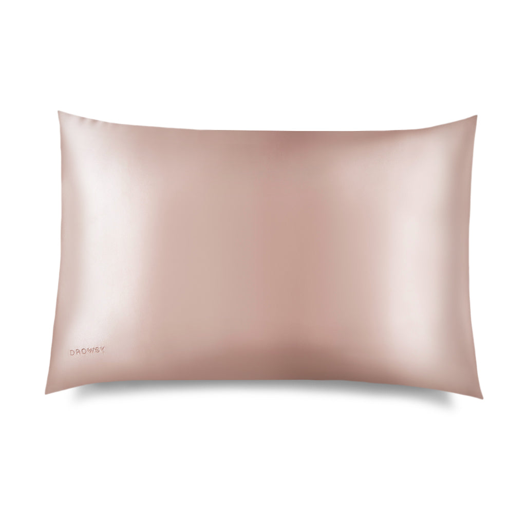 The Sunset Pink Silk Pillowcase by us.drowsysleepco features a smooth, light pink silk finish with a subtle sheen, designed for hair and skin benefits. The small us.drowsysleepco logo is embroidered in one corner on a white backdrop.