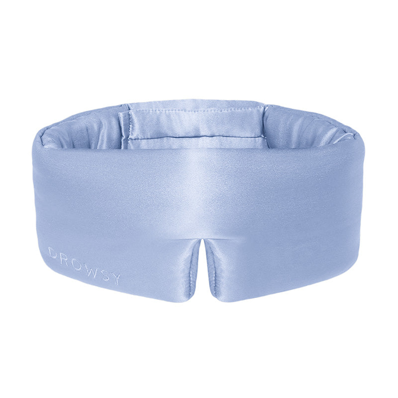 Introducing the Blue Belle eye mask by us.drowsysleepco—a light blue, padded silk mask with a unique wraparound design and a notch at the bottom center. The word "DROWSY" is embroidered on the side. Crafted from smooth silk, this sleep mask helps support skin hydration for a comfortable and restorative night’s rest.