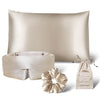 The us.drowsysleepco Sensual Sleep Bundle in Dusty Gold includes a silk pillowcase, sleep mask, scrunchie, and drawstring pouch—luxurious beige accessories displayed on a white background.