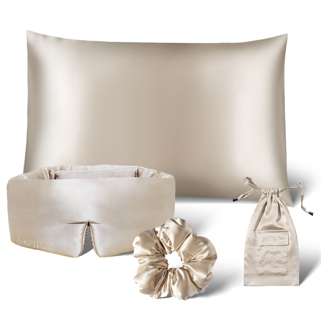 The us.drowsysleepco Sensual Sleep Bundle in Dusty Gold includes a silk pillowcase, sleep mask, scrunchie, and drawstring pouch—luxurious beige accessories displayed on a white background.