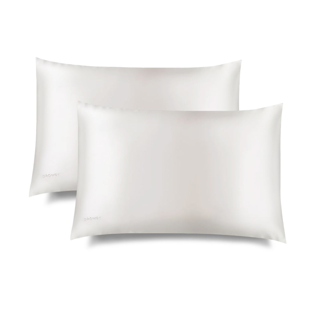 Two white Akoya Pearl Silk Pillowcases (King Size) by us.drowsysleepco are shown overlapping on a white background. Each hair-protecting pillowcase has a smooth, shiny finish and features a subtle logo in the lower left corner.