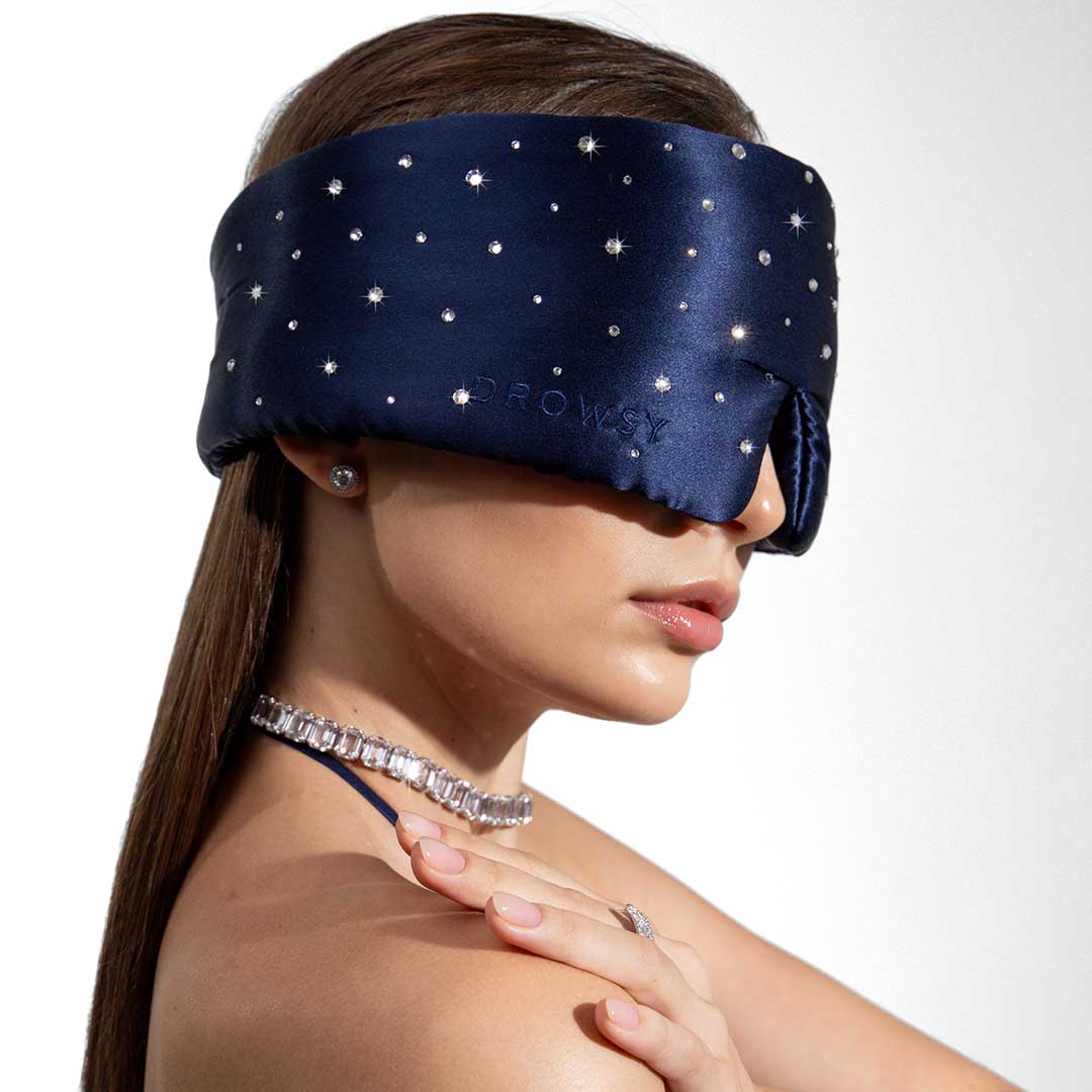 A woman poses against a white background, wearing the us.drowsysleepco Silk Sleep Eye Mask Crystals by Swarovski®, her hand resting on her shoulder.