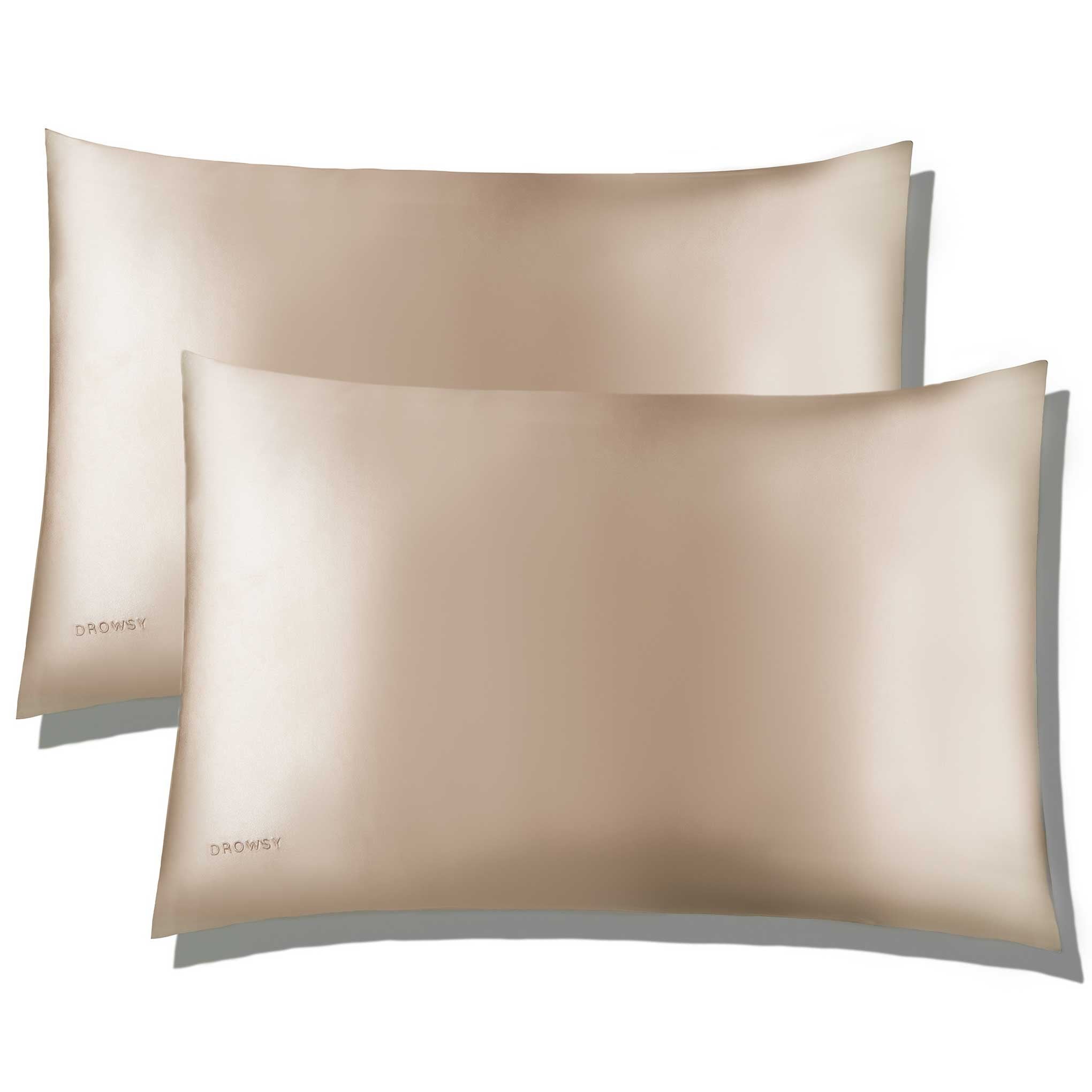 Two Dusty Gold Silk Pillowcases from us.drowsysleepco are arranged with one slightly overlapping the other, showcasing their smooth, shiny texture and subtle DROWSY branding in the lower left corner—perfect for hair and skin care.