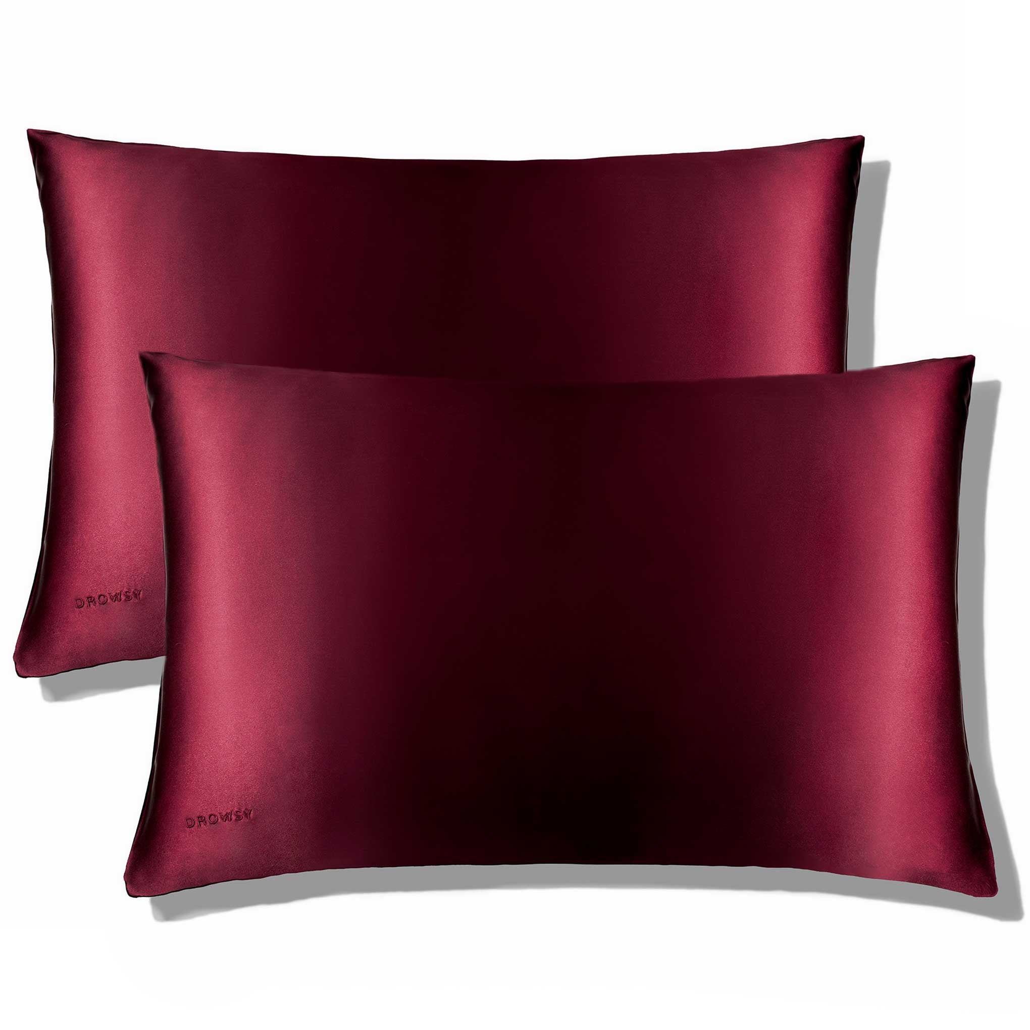 Two rectangular La Vie En Rouge Silk Pillowcases by us.drowsysleepco, in dark red silk with a smooth, shiny texture and “DROWSY” subtly embroidered on the lower corner, are stacked slightly askew against a white background.