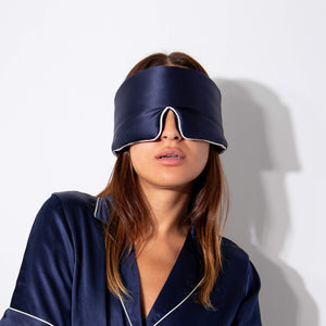 A woman models the us.drowsysleepco Midnight Blue - Pipe Dreams Edition navy satin pajamas and matching blackout silk sleep mask, both covering her eyes and nose, against a plain white background.
