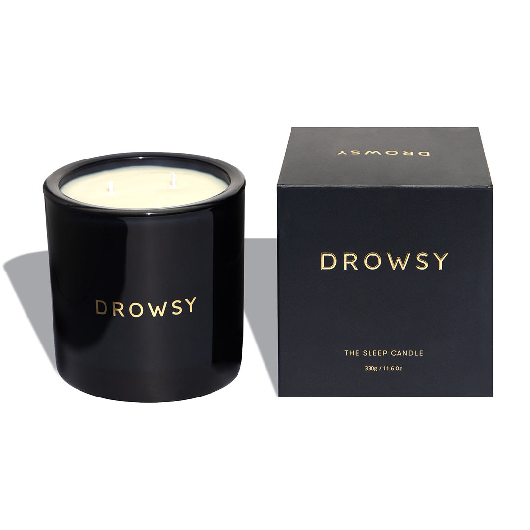 A black candle jar labeled DROWSY sits next to a matching black box with gold text reading DROWSY and THE SLEEP CANDLE, 335g / 11.4oz on a white background.