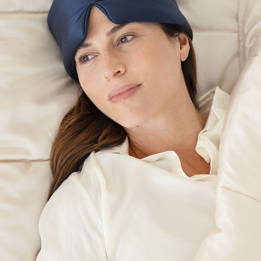 A woman lies in bed with a us.drowsysleepco Dusty Gold Silk Weighted Blanket, looking peaceful and relaxed, embracing deep relaxation for an unrivaled sleeping experience.