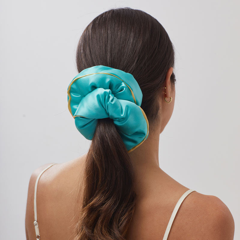 A woman with long brown hair tied in a ponytail, wearing a white top and gold hoops, faces away while using the drowsysleepco Hollywood Experience Bundle - Eyelash protecting.