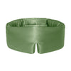 A woman with long dark hair lies on her stomach, resting her head on a white pillow while wearing the Pistachio Green silk eye mask by us.drowsysleepco on her forehead, enjoying a calm moment and looking at the camera.