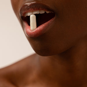 A close-up of a persons smooth-skinned mouth, slightly open and holding a white us.drowsysleepco Supplements - Beauty Sleep Clinic pill between their lips, with a soft, neutral out-of-focus background.
