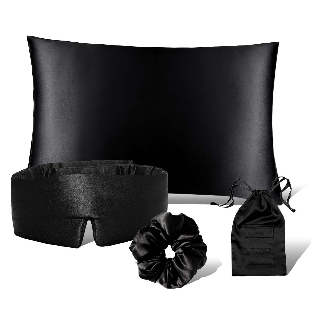 The drowsysleepco Drowsy is the New Black Bundle features a black satin pillowcase, matching silk sleep mask, satin scrunchie, and a small black pouch from the Beauty Sleep Collection, all displayed against a white background.