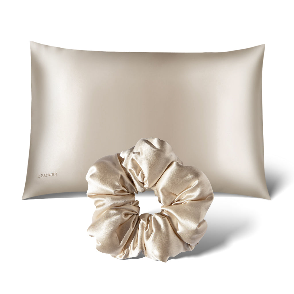 The drowsysleepco Perfect Hair Bundle in Dusty Gold, featuring a light beige silk pillowcase with a subtle sheen and small DROWSY logo, plus a matching silk scrunchie, is displayed on a white background.