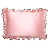 A woman with wavy hair hugs the drowsysleepco Sleep and the City Pink & Black Pillowcase and wears a matching pink satin scrunchie. She has blue eyes, a small geometric wrist tattoo, and is indoors in soft lighting.