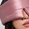 A close-up of a woman wearing the drowsysleepco Damask Rose sleep mask, featuring a Swarovski®-embellished logo, covering her eyes and part of her nose.