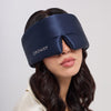A woman with wavy dark hair wears the drowsysleepco Midnight Blue sleep mask, featuring a Swarovski® embellished logo, covering most of her face. She is dressed in a light-colored top.